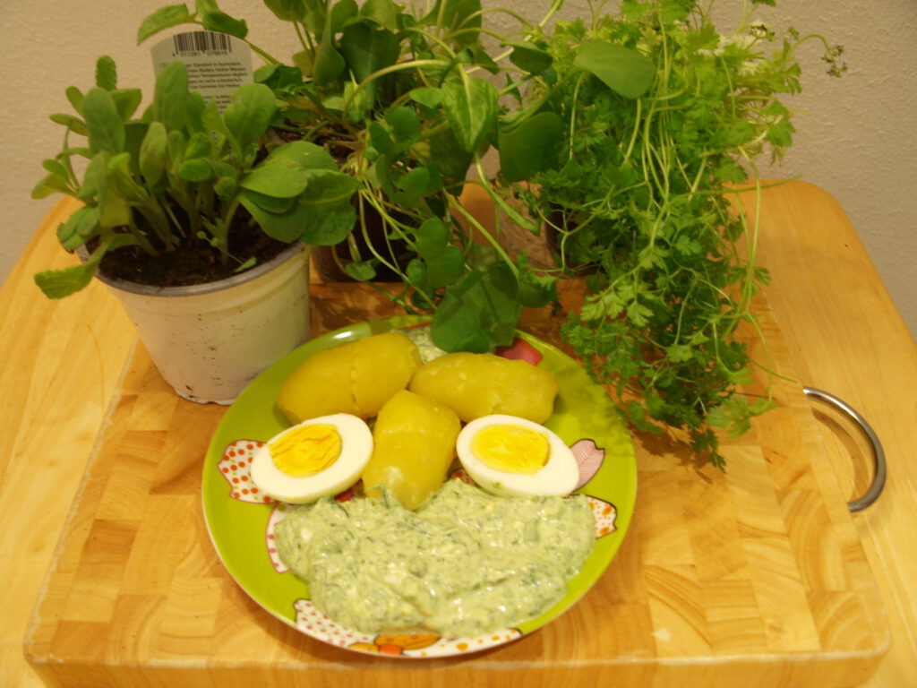 Fertige Frankfurter Grüne Soße mit Dekoration aus Wildkräutern und Teller mit Eiern und Kartoffeln